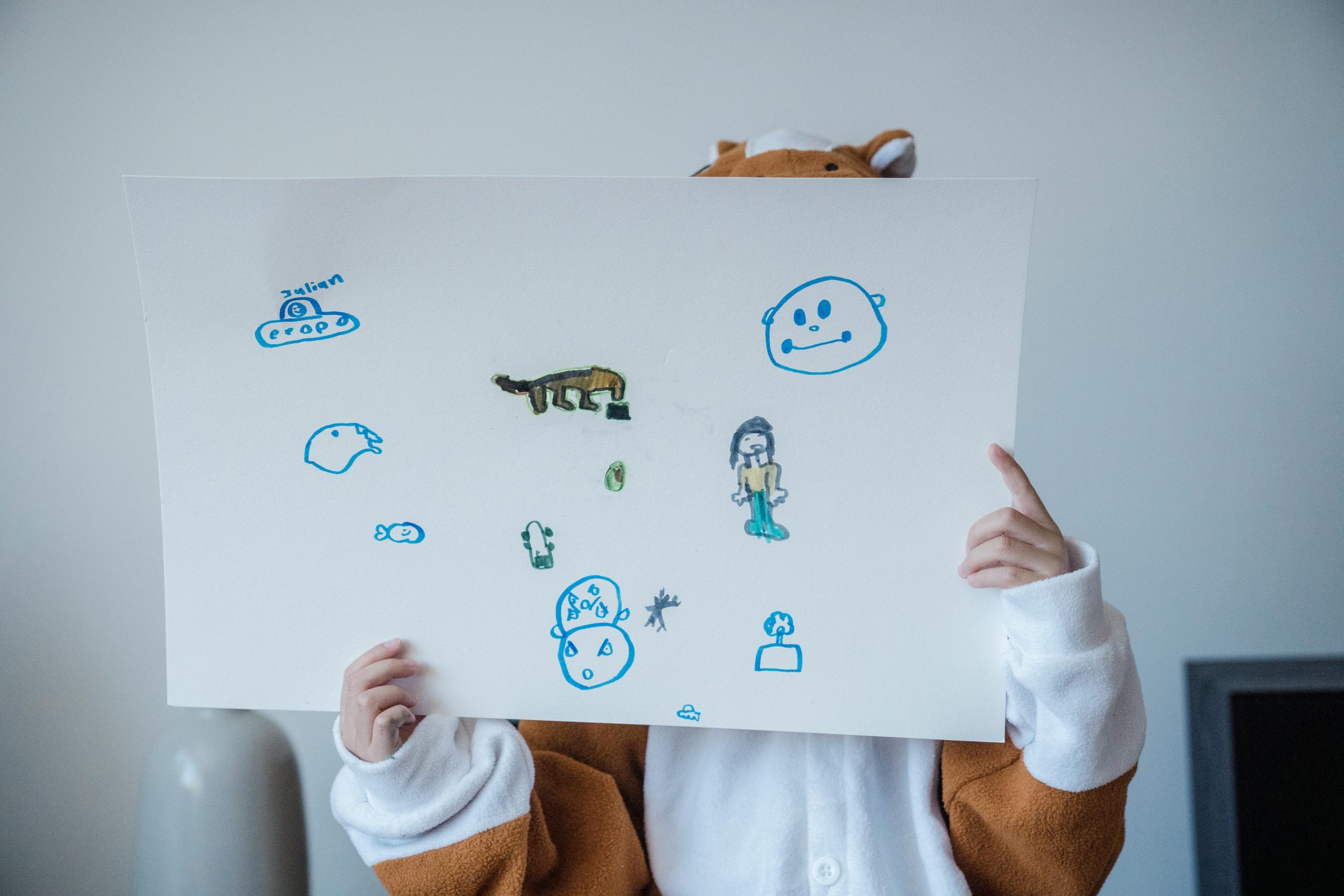 Ses "gribouillis" parlent de lui (et de vous). A child in a costume holds a playful drawing with colorful sketches, expressing creativity.